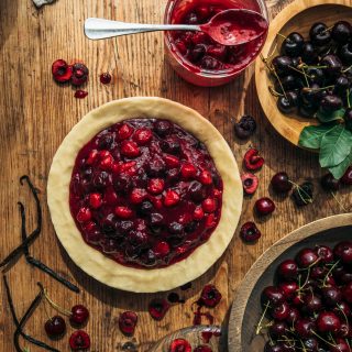 Homemade cherry pie with mixed berries and fresh cherries on a rustic wooden table.