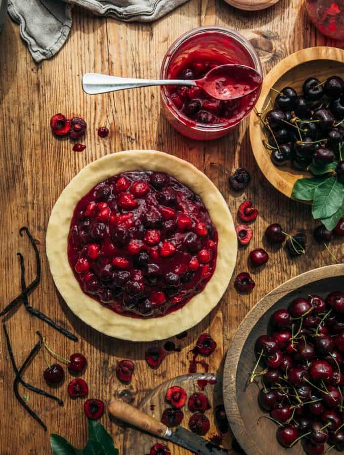 Homemade cherry pie with mixed berries and fresh cherries on a rustic wooden table.